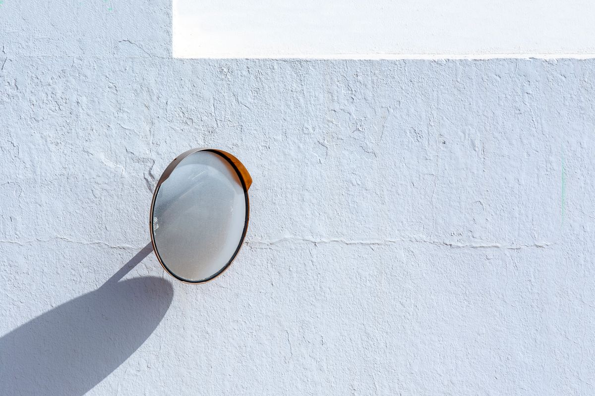 A small round mirror on a pale blue wall, reflecting nothing but light.