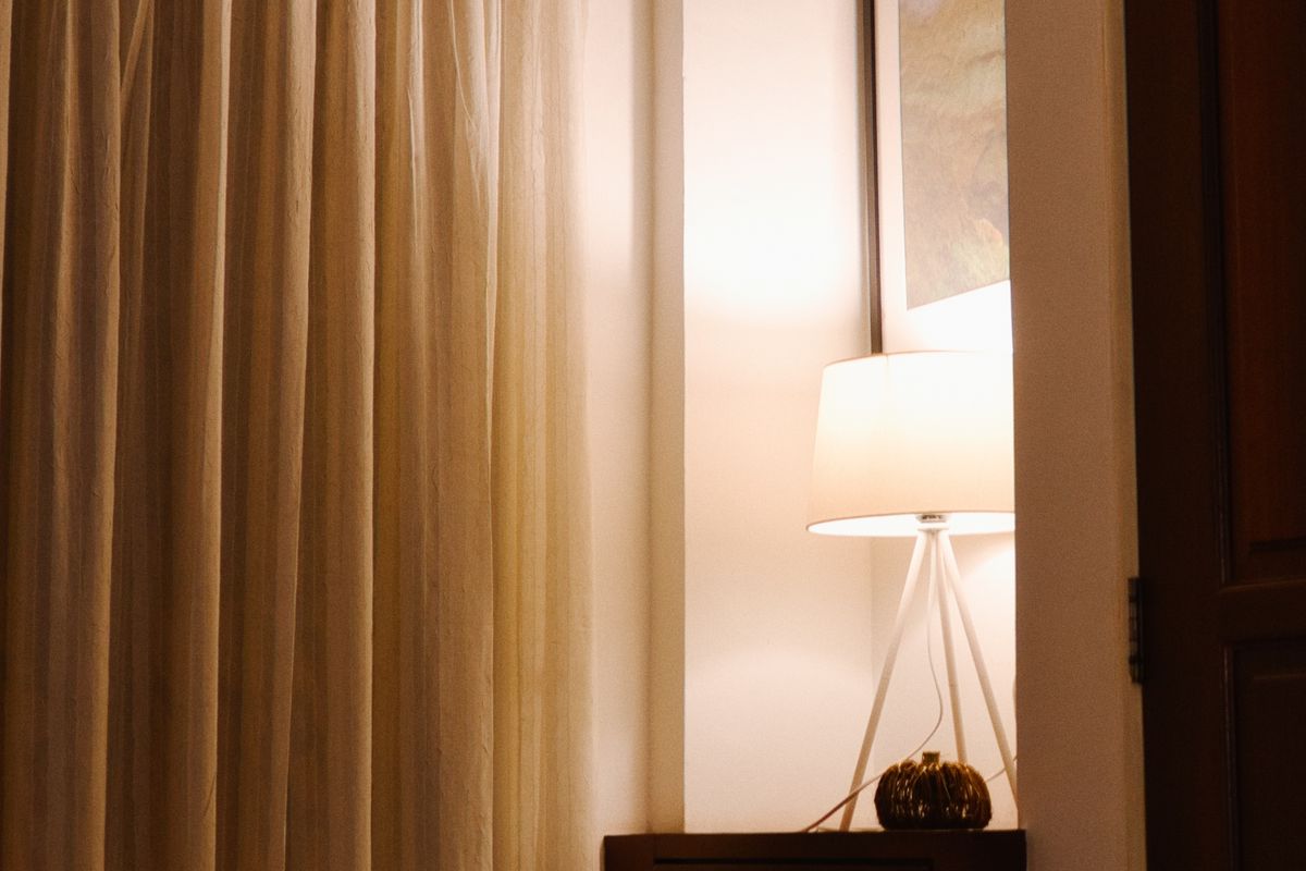 A lit lamp beside drawn curtains in a warm room at dusk.