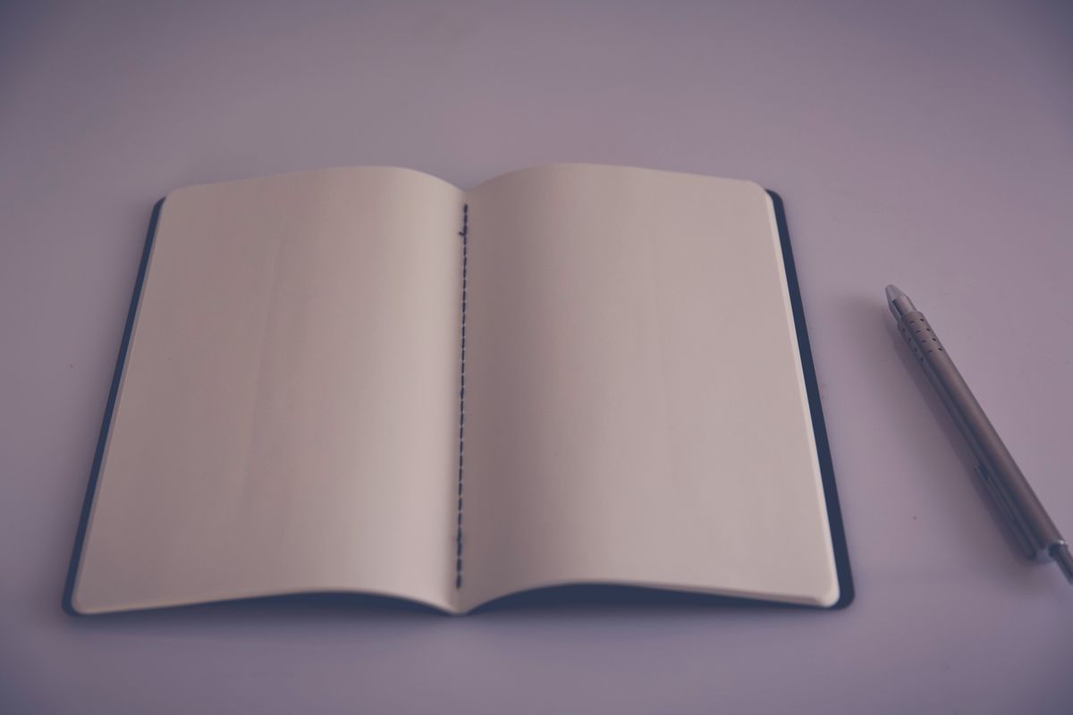 An open notebook with blank pages and a pen, on a lilac surface.
